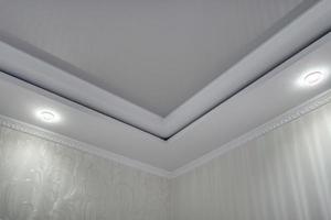 suspended ceiling with halogen spots lamps and drywall construction  with intricate crown molding in empty room in apartment or house. Stretch ceiling white and complex shape. photo