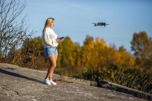 chica controla un dron que se encuentra en una roca alta en las montañas foto