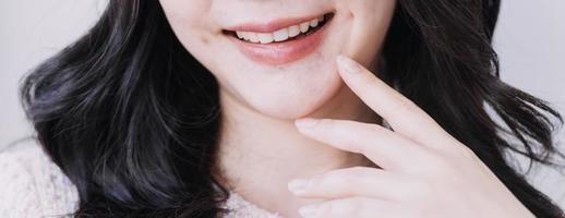 concepto de estomatología, retrato parcial de una chica con fuertes dientes blancos mirando la cámara y sonriendo, con los dedos cerca de la cara. primer plano, de, mujer joven, en, dentista, estudio, adentro foto