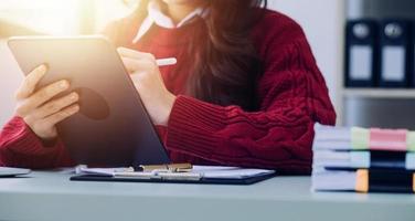 Young business woman sitting in office at table and using smartphone. On desk is laptop and tablet computer, on screen charts and graphs. Woman analyzing data. Student learning online. photo