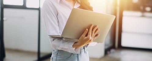 Woman hand using smart phone and laptop in outdoor nature park and sunset sky with bokeh light abstract background. Technology business and freelance working concept. Vintage tone filter color style. photo