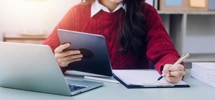 Young business woman sitting in office at table and using smartphone. On desk is laptop and tablet computer, on screen charts and graphs. Woman analyzing data. Student learning online. photo