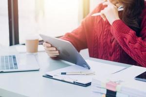 Young business woman sitting in office at table and using smartphone. On desk is laptop and tablet computer, on screen charts and graphs. Woman analyzing data. Student learning online. photo