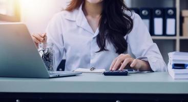 Young business woman sitting in office at table and using smartphone. On desk is laptop and tablet computer, on screen charts and graphs. Woman analyzing data. Student learning online. photo