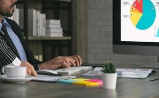 Two business colleagues working in office and using computer. Man sitting at his desk with female colleague standing besides him photo