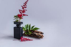 Beautiful bottle of men's perfume or toilet water on a gray background with flowers and tree bark. A blank layout for the product presentation.