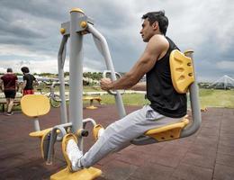 Sportsman working out on the sports public equipment in the outdoor gym. A sportive active man in a park at cloudy day. photo