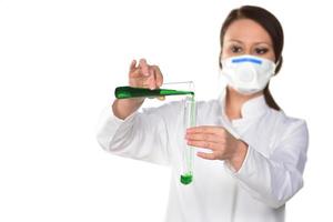 Scientist with white mask holding two tubes transferring green liquid from one to another. photo