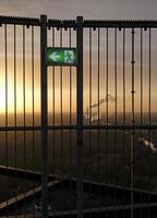 An emergency exit sign with an industrial site in the background during sunset photo