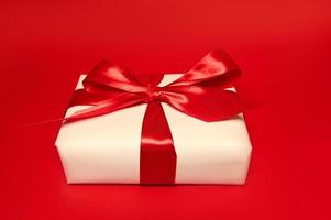 A gift box with big red bow against red background. Holidays concept photo