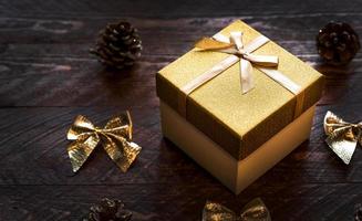 Closeup of shiny golden gift box on wooden table with bows and cones near. Christmas or new year banner photo