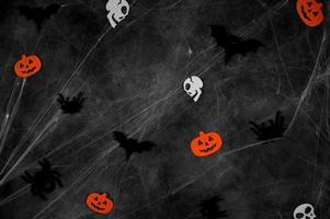 murciélagos voladores negros, arañas, calaveras y calabazas en la web sobre fondo de hormigón oscuro foto