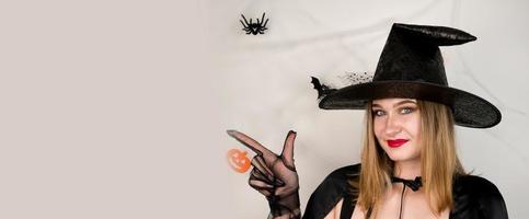 banner de copyspace de halloween con hermosa rubia en un disfraz de bruja apuntando al espacio vacío. invitación de fiesta. foto