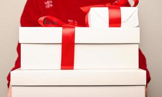 Woman in red sweater holding a pile of white gift boces with red bows. photo