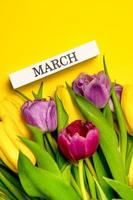 pancarta de resorte vertical. un ramo de tulipanes amarillos, rosas y morados y marcha escrita en un bloque de madera. concepto del día de la mujer foto