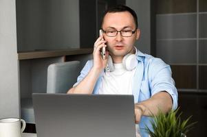 hombre asiático con teléfono y computadora portátil. sentarse y hablar por teléfono inteligente pidiendo algo o discutiendo algo con el cliente. foto