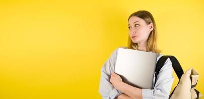 Portrait of tired young female with laptop with confused puzzled face on yellow isolated background. Studio shot photo