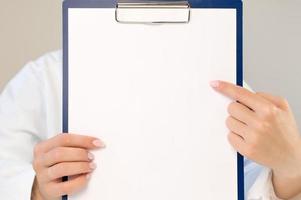 A doctor in a white coat points to an empty space on a paper. The doctor is holding a folder with an empty sheet in his hands. Space for copy and records. Medical concept.Copy space photo