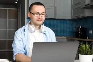 Asian smiling male in glasses uses laptop for shopping,programming,working etc.Modern technologies concept photo