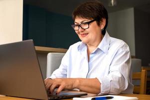 Happy elder woman wearing glasses uses laptop for work,education,communication etc photo