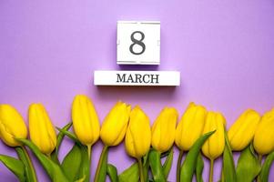 8 de marzo tendido plano. calendario con fecha yace rodeado de tulipanes amarillos foto