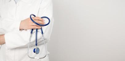 un médico con una bata médica blanca sostiene un estetoscopio en sus manos. concepto de salud. banner con lugar para texto
