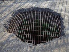 Old hole in the concrete floor covered with grating. Trap. Cell in the dungeon. photo