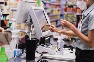 mujer con mascarilla en el mostrador de pago manos del cajero escanea comestibles en el supermercado. foto