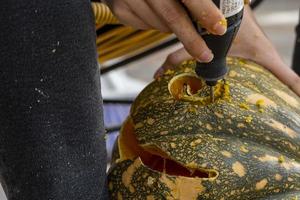 young man with a drill or dremel drilling a pumpkin for halloween photo