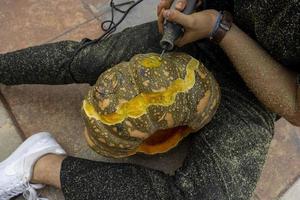 young man with a drill or dremel drilling a pumpkin for halloween photo