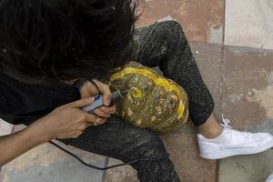 young man with a drill or dremel drilling a pumpkin for halloween photo