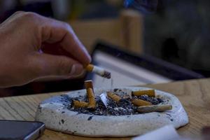 young man smoking on a wooden table, ashtray with several used cigars, mexico photo