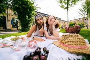 Two women having picnic together, laying on the park lawn photo