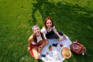 Two women having picnic together, sitting on the plaid photo