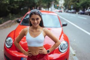 Portrait of pretty Caucasian woman standing against new red car photo