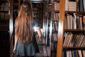 vista trasera. una estudiante está en una biblioteca llena de libros. concepción de la educación foto