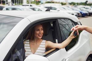 Taking keys of the car. Two people. Girl sitting in her brand new automobile photo