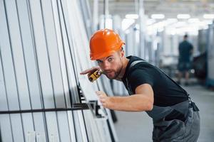 Measuring length of objects. Industrial worker indoors in factory. Young technician with orange hard hat photo