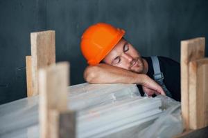 Sleeping on a job. Taking a break. Industrial worker indoors in factory. Young technician with orange hard hat photo