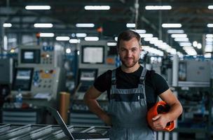 trabajador industrial en el interior de la fábrica. joven técnico con casco naranja foto