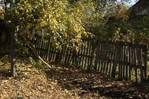 valla en el pueblo en otoño. antigua valla de madera en el jardín. jardín en el pueblo. foto