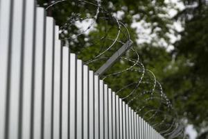 Steel fence with barbed wire. Fence around plant. Private territory. Metal profile. Dangerous wire. photo