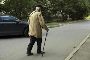 Old man with walking stick walks down road. Retired in Russia. Elderly man with gray hair. Poor man. photo