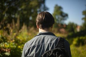 Guy walks through woods. Man from behind in summer. Young man came to village. photo