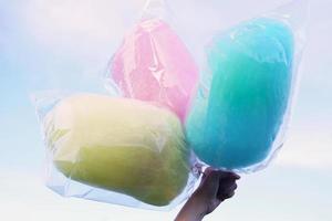 Three bags of cotton candy in three colors. Hold in hand on sky background. Cotton candy made from sugar spun into thin noodles. Like a cloud, many colors depending on the color photo