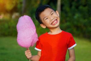 Asian boy holding pink cotton candy in hand, cheerful smile, happy to eat. It made the sugar churned into thin, cloud-like lines, with different colors depending on the color. photo