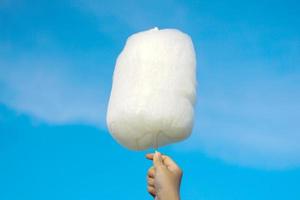 holding white cotton candy on sky background. Cotton candy made from sugar spun into thin noodles. Like a cloud, many colors depending on the color. Soft and selective focus photo