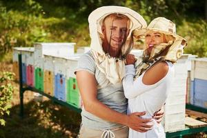 Portrait of two lovely beekeepers. Stands together near the hives. Sweet couple embracing photo