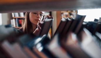 ver a través de los estantes. una estudiante está en una biblioteca llena de libros. concepción de la educación foto