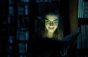 misteriosa luz verde proviene del libro. concepción de la creatividad. estudiante femenina está en la biblioteca. concepción de la educación foto